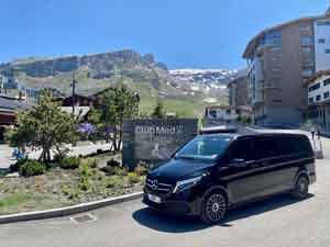 VTC-haut-de-gamme-en-savoie Mercedes classe V noir stationné devant l'entrée du club Med de Tignes avec en fond la montagne ensoleillée